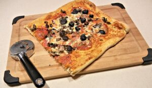Pizza fatta in casa con pasta leggera, lievitata 48 ore, su tavolo di legno con ingredienti freschi.