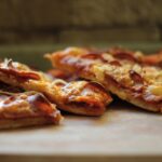 Pizza in teglia con bordi bassi, evidenziando la mancanza di lievitazione e la consistenza densa.