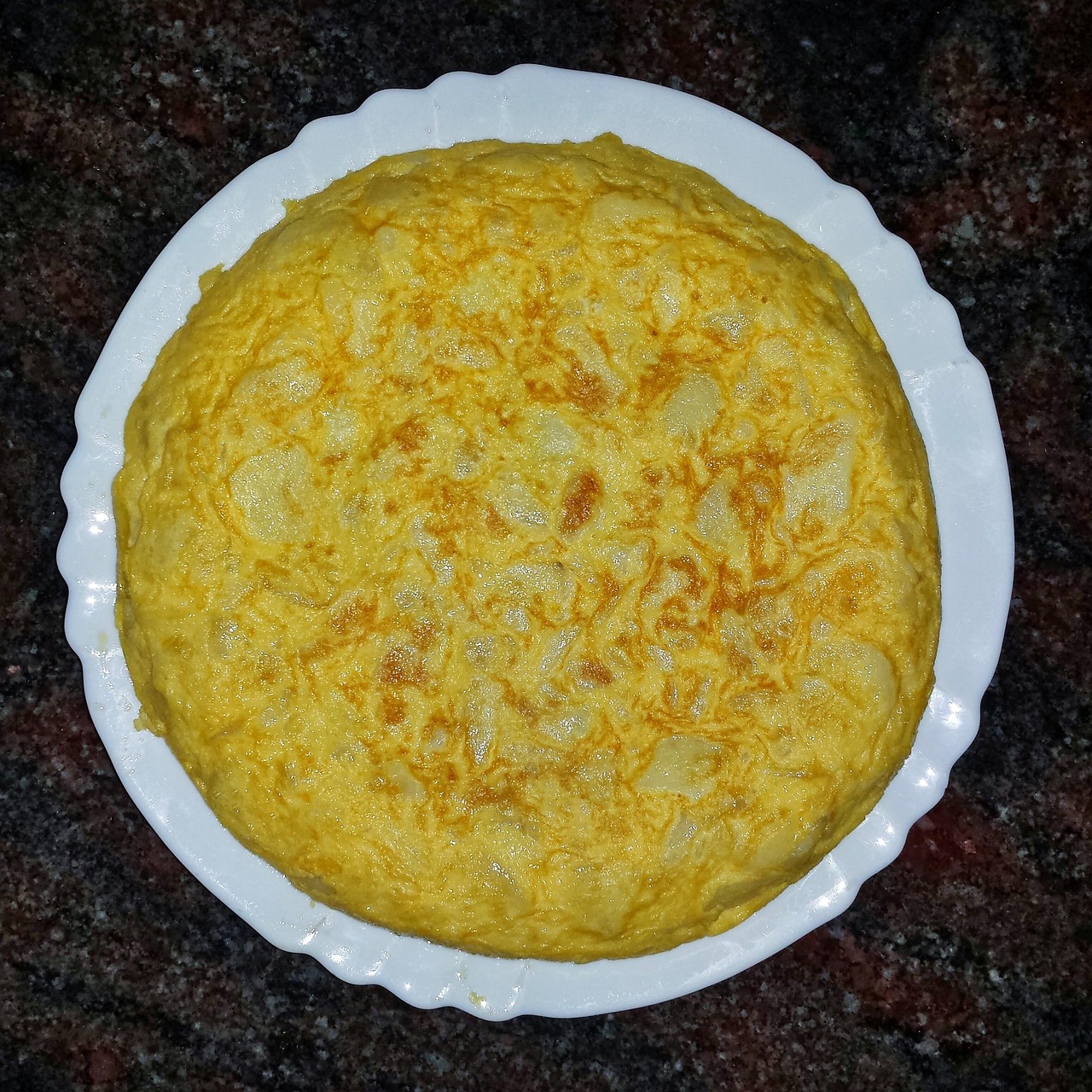 Frittata alta e soffice appena sfornata, servita su un piatto bianco.